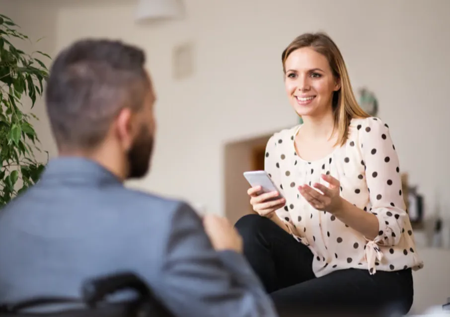A woman sitting and talking with a colleague, gesturing as she speaks, in a relaxed one-to-one conversation.